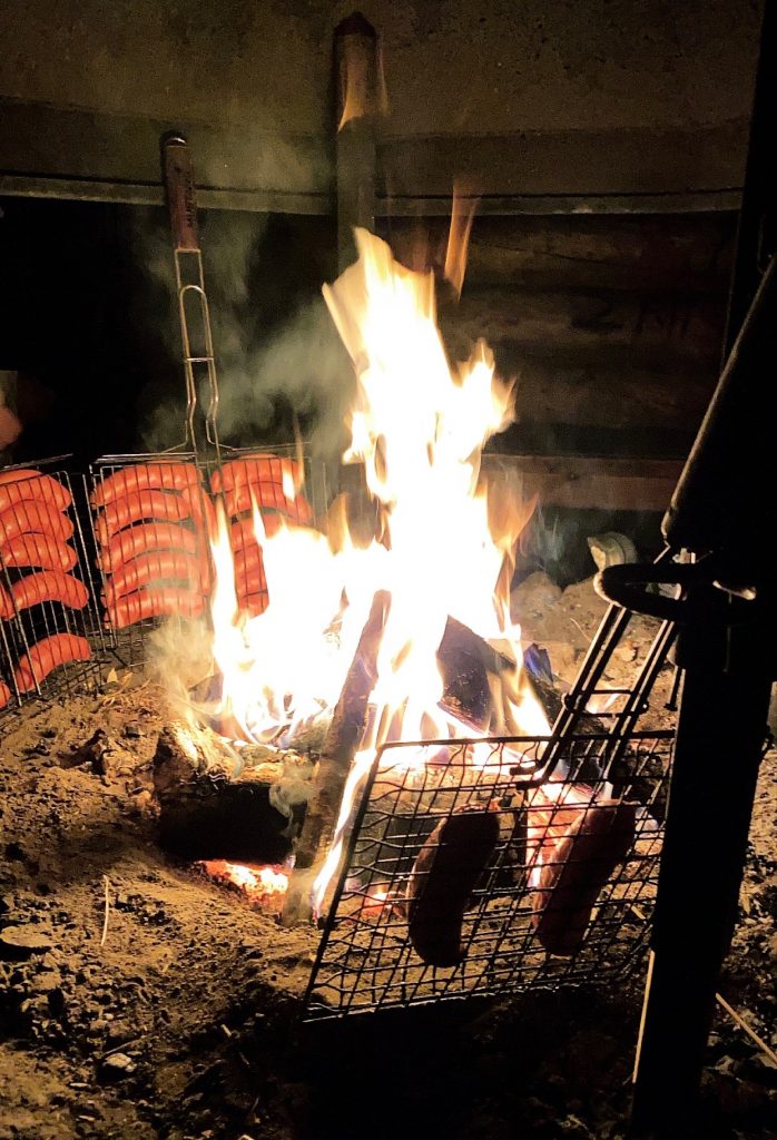 Photo of a campfire with sausages cooking.