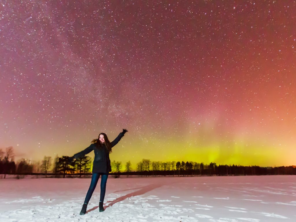 Photo of a woman standing in front of the Northern Lights.