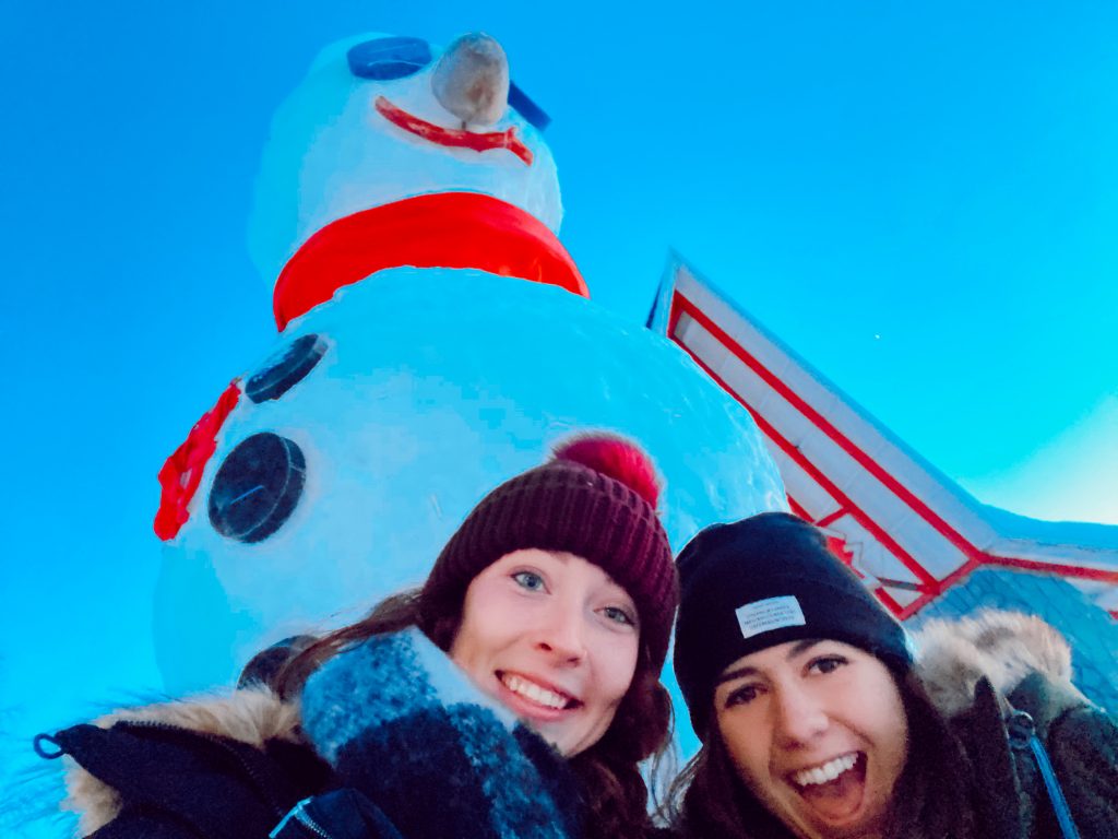 Photo of two women standing in front of a towering snowman.