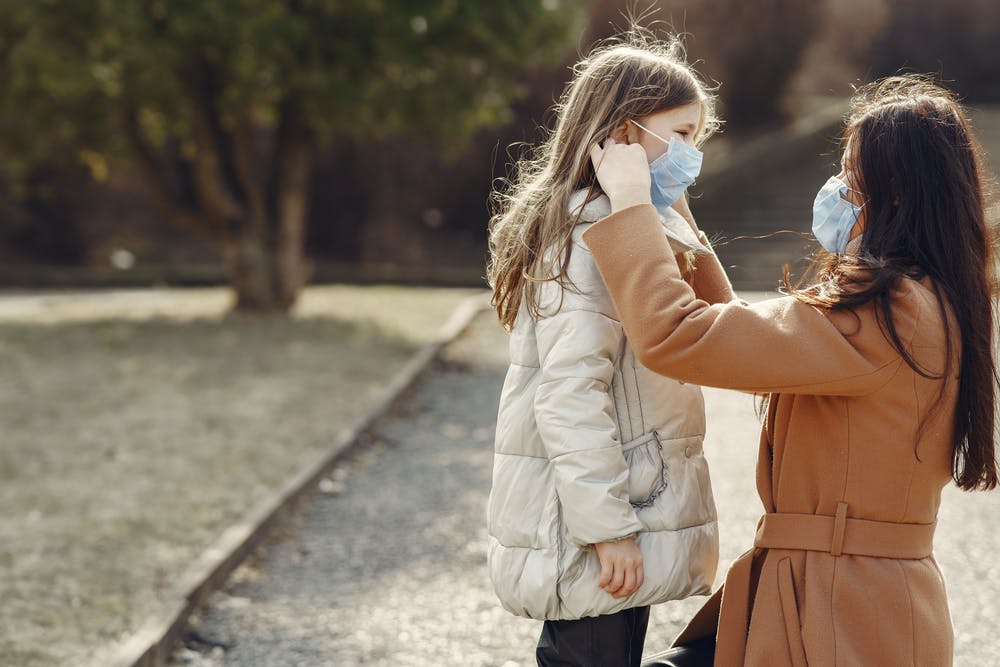 Woman adjusting a childs protective mask while she wears one herself.