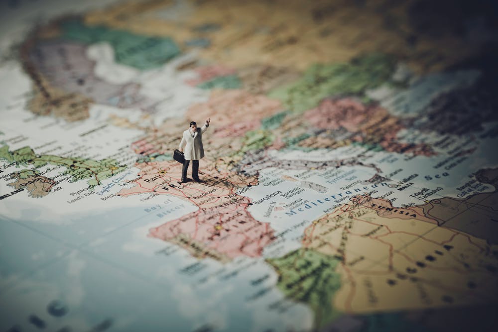 Photo of a man standing on a world map that is proportionally much bigger than him.