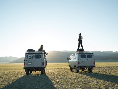 Two people standing on top of their vans in a silhouette shadow.